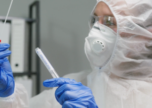 A person in protective lab wear, including a mask and gloves, is handling a test tube in an Auto Draft laboratory environment.