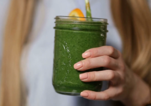 A person holding a jar of green smoothie with a slice of orange on the rim
